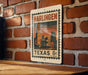 A metal sign with a vintage-style illustration of Harlingen, Texas, mounted on a brick wall.