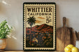 A vintage-style stamp depicting Whittier, California, with a palm tree and mountains in the background, placed on a shelf next to a wooden cutting board and some lemons.