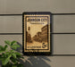 A vintage postage stamp from Tennessee, featuring an old street scene, is mounted on a wall next to a plant.