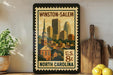 A framed vintage postage stamp depicting the Winston-Salem, North Carolina area, with a cityscape and a church.