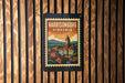 A vintage-style postage stamp depicting a town with a church, hanging on a wooden wall.