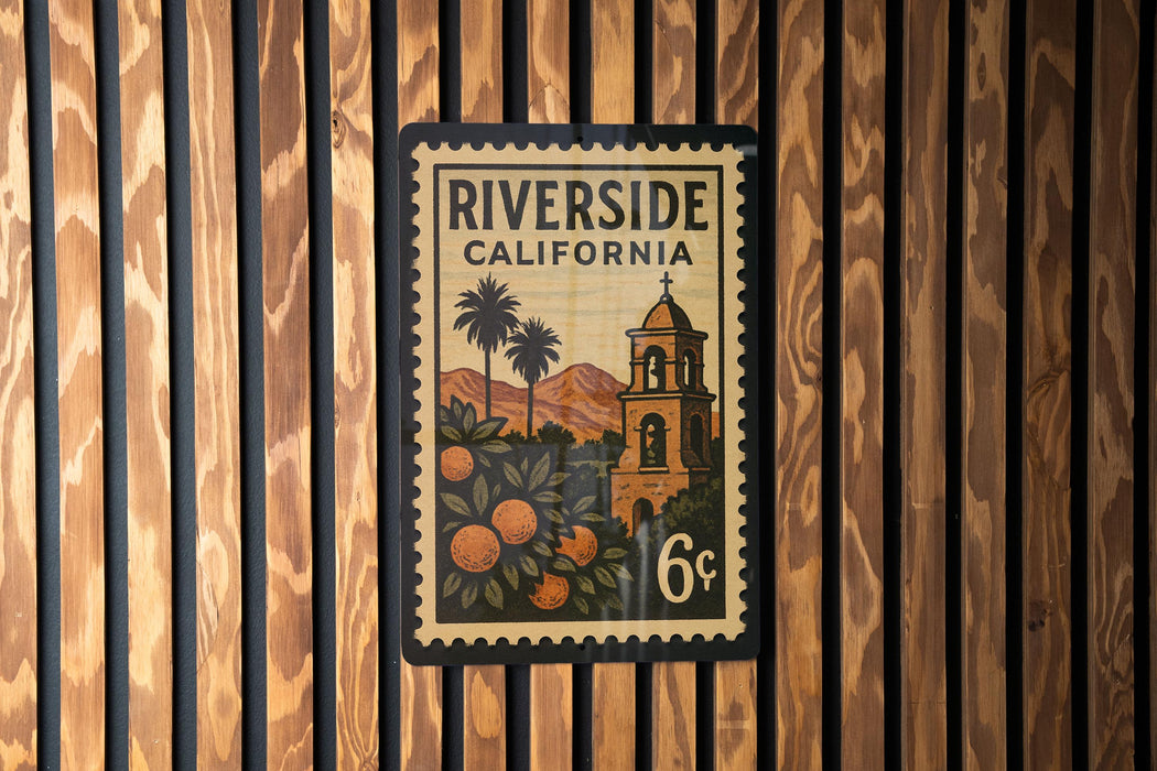 A vintage postage stamp from Riverside, California, featuring a bell tower and palm trees, mounted on a wooden wall.