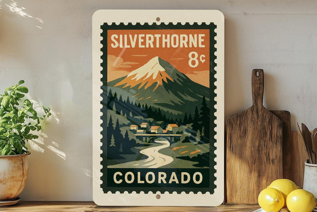 A vintage-style postage stamp from Colorado, featuring a mountain landscape with a small village in the foreground.