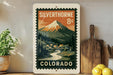 A vintage-style postage stamp from Colorado, featuring a mountain landscape with a small village in the foreground.