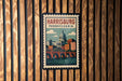 A vintage-style postage stamp depicting the Harrisburg, Pennsylvania skyline, with a bridge and dome in the center.