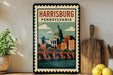 A framed poster of Harrisburg, Pennsylvania, featuring a cityscape with a bridge and dome, is displayed on a wall next to kitchen utensils and a potted plant.