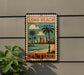 A vintage-style metal sign with a beach scene and palm trees, mounted on a wall, with a plant to the left.