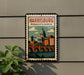 A framed poster of Harrisburg, Pennsylvania, featuring a cityscape with a bridge and dome, mounted on a wall.