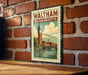 A vintage-style metal sign with the text "WALTHAM MASSACHUSETTS" and an illustration of a clock tower and a bridge, mounted on a brick wall.