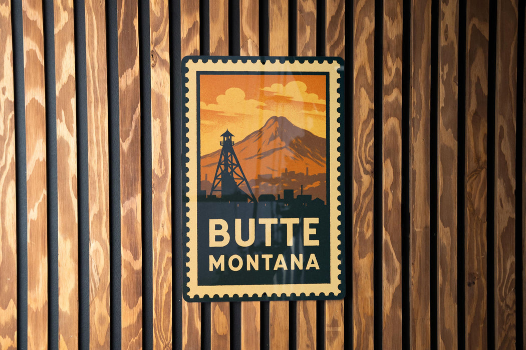 A vintage-style metal sign with the text "BUTTE MONTANA" displayed prominently against a wooden background.