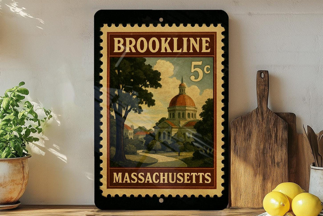 A vintage-style postage stamp from Massachusetts featuring a building and trees, placed on a wooden surface next to a wooden cutting board and a potted plant.