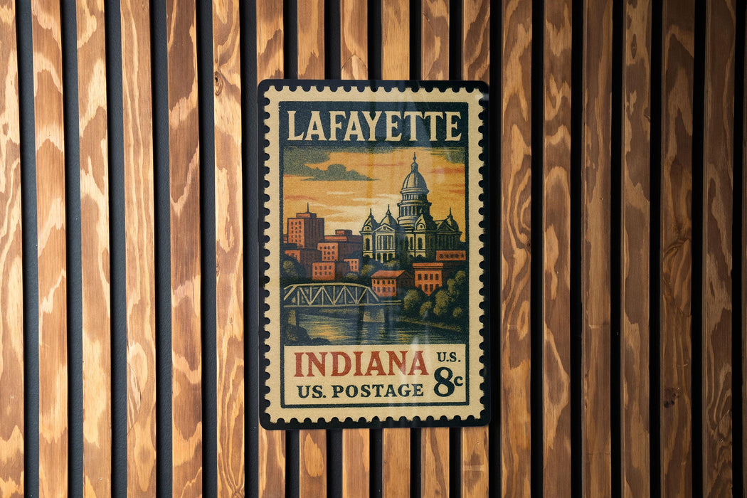 A vintage postage stamp from Lafayette, Indiana, featuring a cityscape and a bridge, is displayed on a wooden wall.
