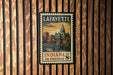 A vintage postage stamp from Lafayette, Indiana, featuring a cityscape and a bridge, is displayed on a wooden wall.