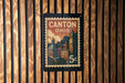 A postage stamp depicting Canton, Ohio, with a cityscape and a clock on a wooden background.