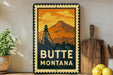A vintage-style metal sign with a mountain and a tower in the background, along with the text "BUTTE MONTANA" displayed prominently.