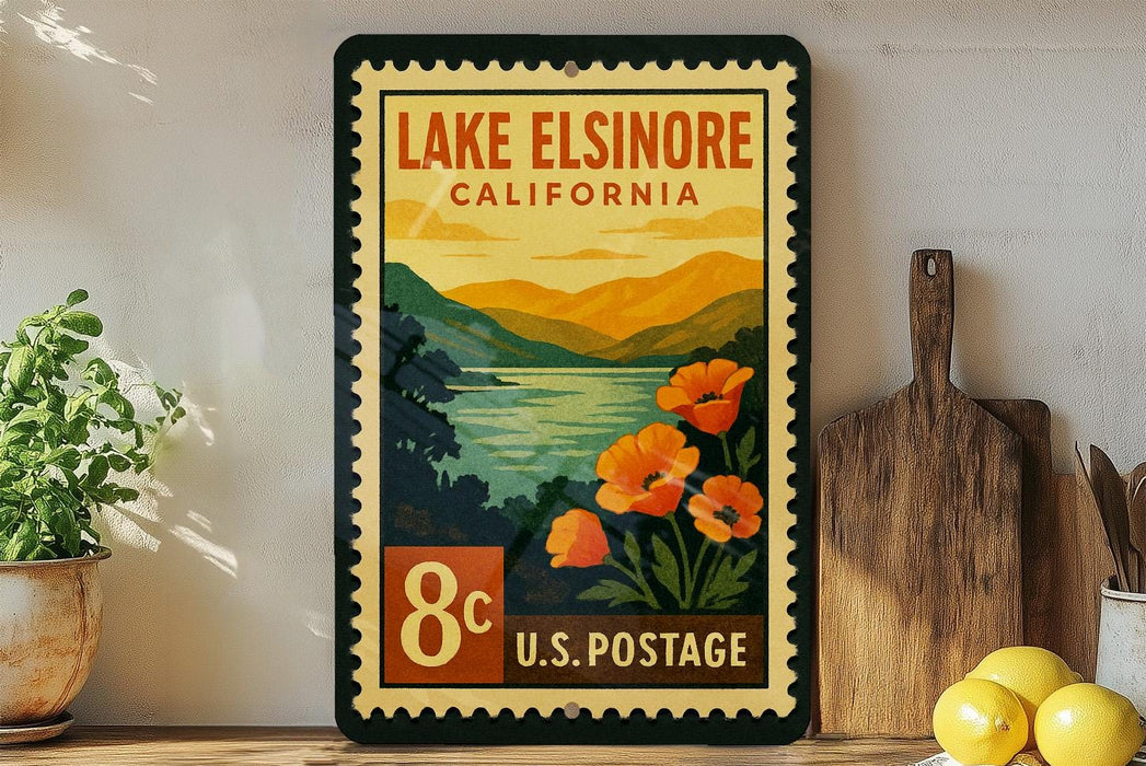 A vintage-style postage stamp from Lake Elsinore, California, featuring a scenic landscape with mountains, a lake, and orange flowers.