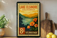A vintage-style postage stamp from Lake Elsinore, California, featuring a scenic landscape with mountains, a lake, and orange flowers.