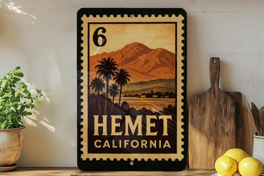 A framed stamp-like artwork depicting a scenic landscape with palm trees and mountains, hanging on a wall next to a wooden cutting board and a potted plant.