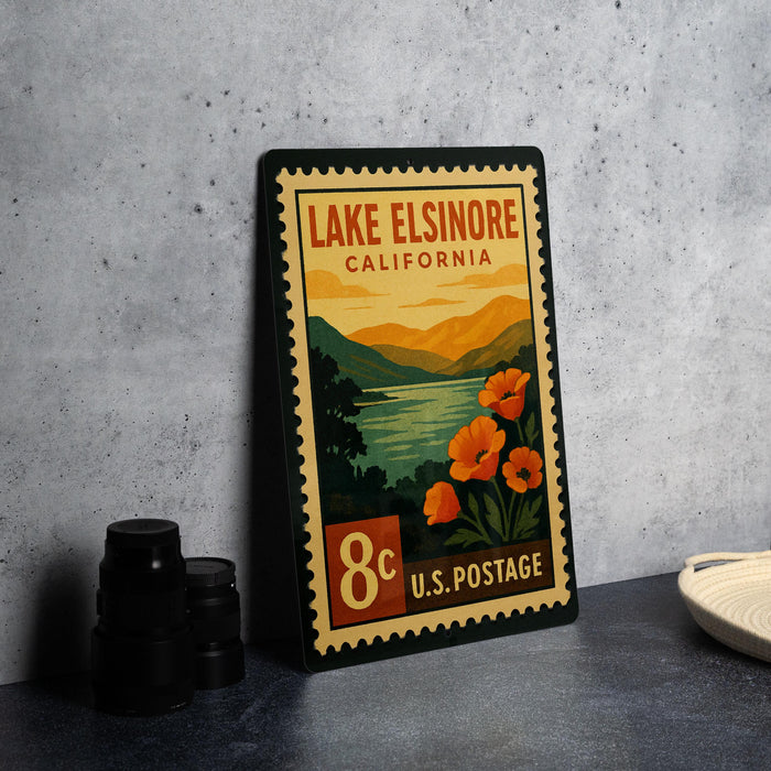 A vintage-style postage stamp from Lake Elsinore, California, featuring a scenic landscape with mountains, a lake, and orange flowers.