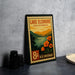 A vintage-style postage stamp from Lake Elsinore, California, featuring a scenic landscape with mountains, a lake, and orange flowers.