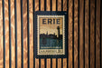 A vintage-style postage stamp from the United States, featuring the city of Erie, Pennsylvania, with a lighthouse and a sailboat in the background.