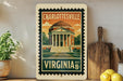 A vintage-style postage stamp depicting the University of Virginia, with a building and a tree in the background, hangs on a wall next to a wooden cutting board and a potted plant.