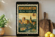 A framed vintage postage stamp from New York, featuring a cityscape and a bridge, is displayed on a shelf next to a wooden cutting board and some lemons.