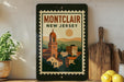 A framed poster of Montclair, New Jersey, featuring a colorful illustration of the town's buildings and landscape.