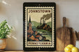 A framed poster of Johnstown, Pennsylvania, featuring a stylized illustration of the town with steam rising from the buildings.