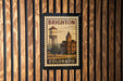 A vintage postage stamp from Brighton, Colorado, featuring a water tower and a building, is displayed on a wooden wall.