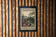 A vintage-style postage stamp from Pennsylvania, featuring a town scene with a church and steam-powered factory, is displayed on a wooden wall.