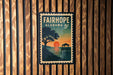 A vintage-style postage stamp from Alabama, featuring a sunset over a body of water with a pier and a tree in the foreground.