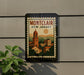 A framed poster of a town in New Jersey, featuring a bell tower and other buildings, is displayed on a wall next to a plant.