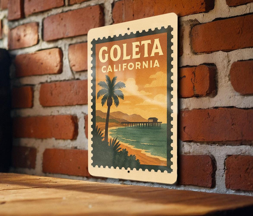 A vintage-style metal sign with the text "GOLETA CALIFORNIA" and an illustration of a palm tree and a beach with a pier in the background, mounted on a brick wall.