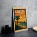 A vintage-style metal sign with the text "GOLETA CALIFORNIA" and an illustration of a palm tree and a pier, placed on a gray countertop next to some black camera lenses.