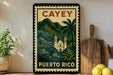 A vintage-style poster of the Cayey region in Puerto Rico, featuring a church and palm trees, is displayed on a wall next to a wooden cutting board and a potted plant.