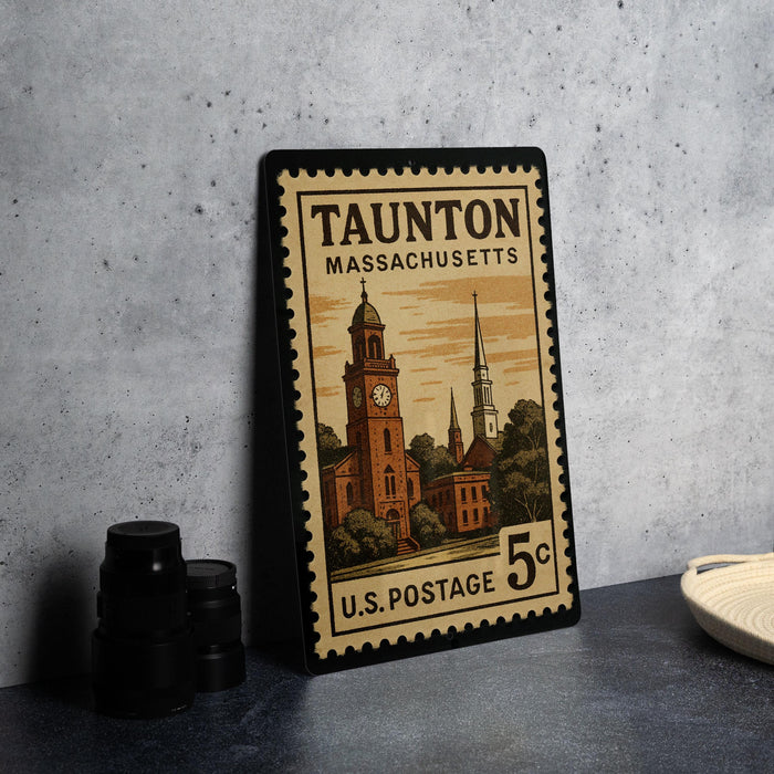 A vintage Massachusetts postage stamp featuring a clock tower and other architectural elements, placed on a countertop next to some camera equipment.