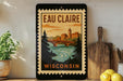 A framed poster of a scenic view of Wisconsin, featuring a bridge, trees, and a river, is displayed on a shelf next to a wooden cutting board and some lemons.