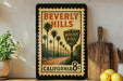 A framed vintage-style poster of Beverly Hills, California, featuring palm trees and a road, is displayed on a shelf next to a wooden cutting board and some lemons.