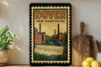 a vintage-style poster of Dover, New Hampshire, with a waterfall and buildings in the background, displayed on a wall next to a wooden cutting board and some lemons.