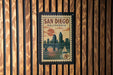A vintage-style postage stamp from San Diego, California, featuring a cityscape and a sailboat, mounted on a wooden wall.