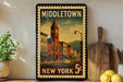 A vintage-style metal sign with a colorful illustration of a town, featuring a clock tower, buildings, and a street scene, mounted on a wall next to a wooden cutting board and some potted plants.
