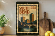 A framed poster of the city of Bend, Indiana, with a bridge and buildings in the background, displayed on a wall next to a wooden cutting board and some lemons.