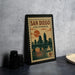 A framed poster of San Diego, California, featuring a cityscape and a sailboat, is displayed on a table.