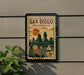 A framed poster of San Diego, California, featuring a cityscape and a sailboat, is displayed on a wall.