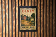 A vintage-style postage stamp from Maryland, featuring a rural landscape with a barn and a road, is displayed on a wooden wall.