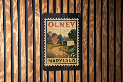 A vintage-style postage stamp from Maryland, featuring a rural landscape with a barn and a road, is displayed on a wooden wall.