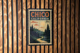 A vintage-style postage stamp from California, featuring a scenic landscape with pine trees, a winding road, and a sunlit sky.