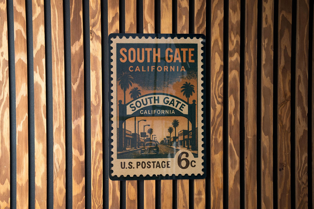 A vintage postage stamp from the United States, featuring a street scene with palm trees and buildings, mounted on a wooden wall.