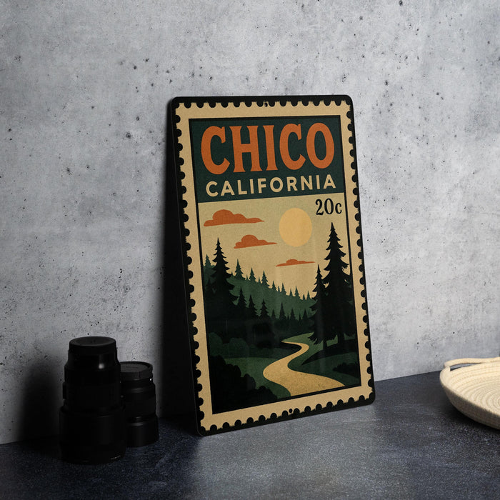A vintage-style metal stamp with the text "CHICO CALIFORNIA" and a landscape scene depicting a winding road, pine trees, and a sunset.